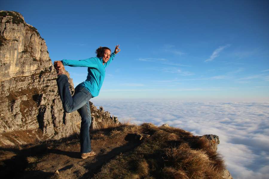 Birgit Peer in Tänzerpose auf einem Felsgrat, unter ihr ein Meer aus Wolken